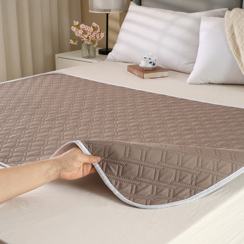 Person holding a quilted mattress protector over a bed in a bedroom setting.