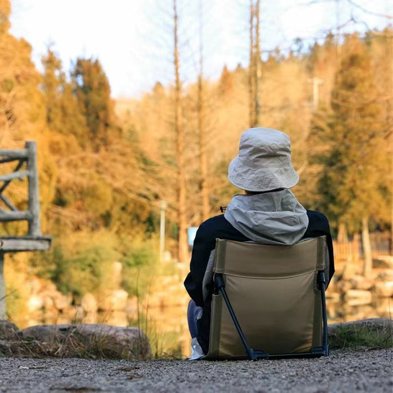 Person sitting in a folding chair by a lake with trees in the background
