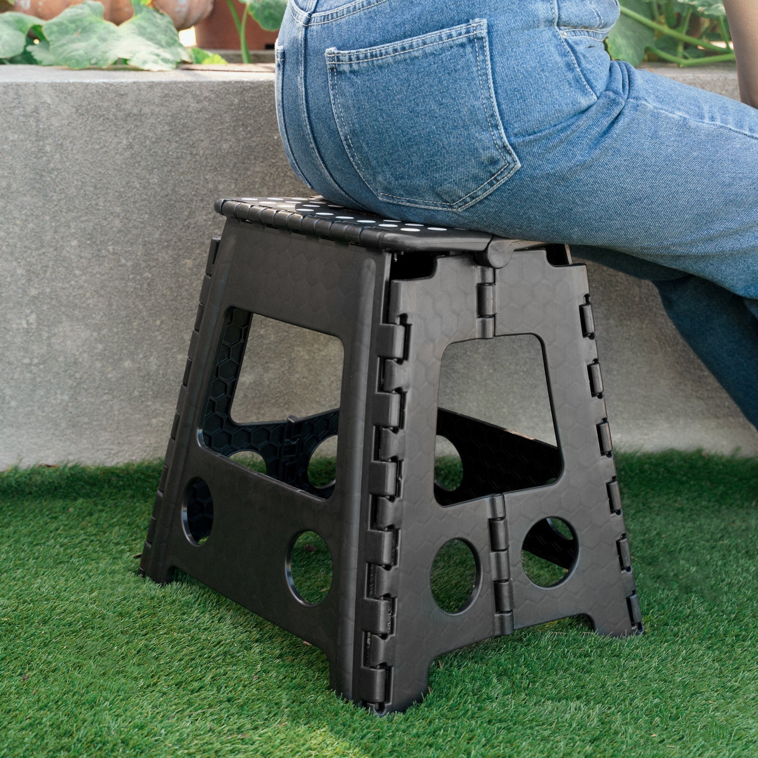 Black folding stool on grass with a person wearing blue jeans in the background