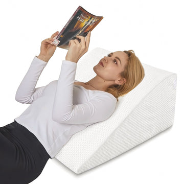 Woman lying on a wedge-shaped foam pillow reading a book.