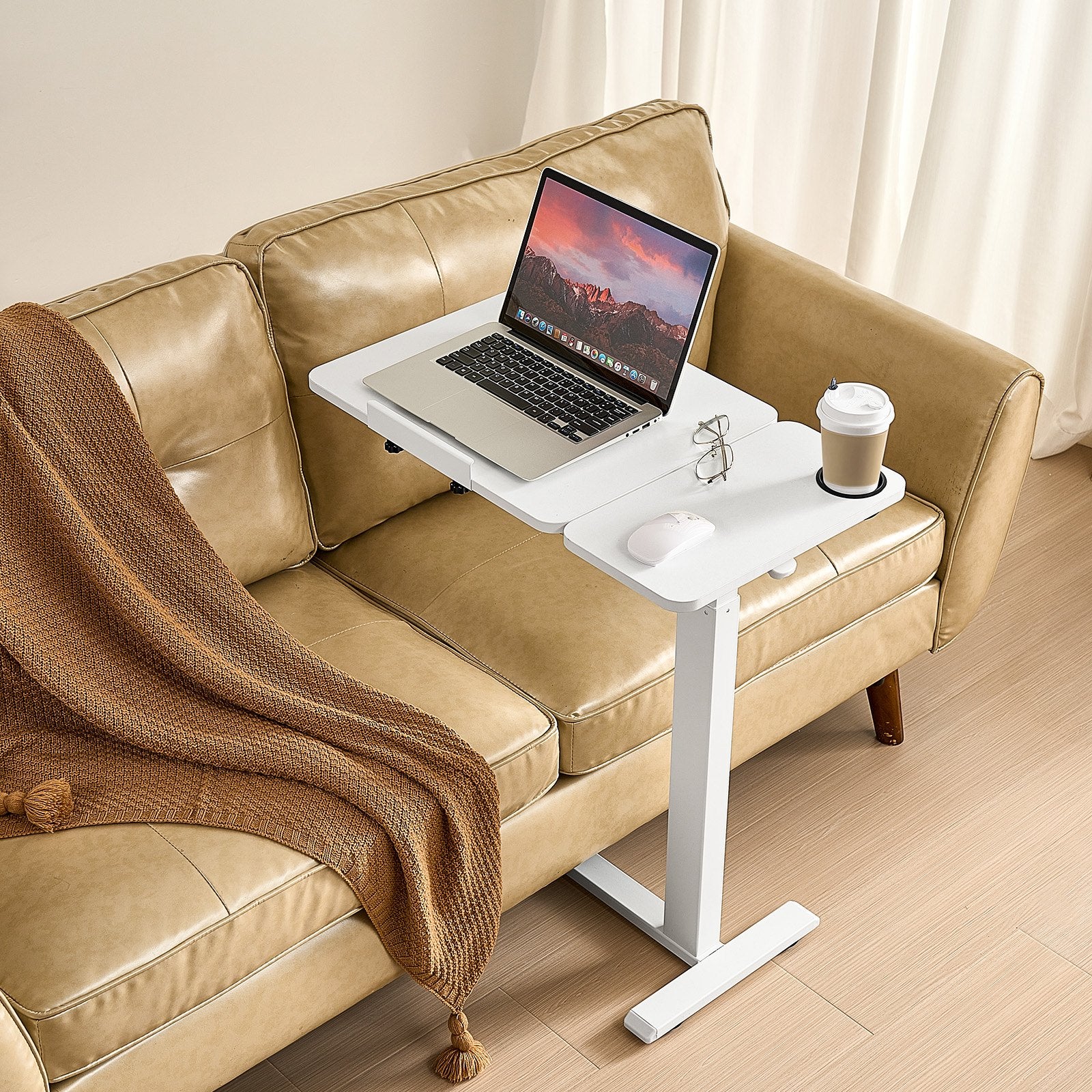 Laptop on a white adjustable table on a beige sofa with a blanket