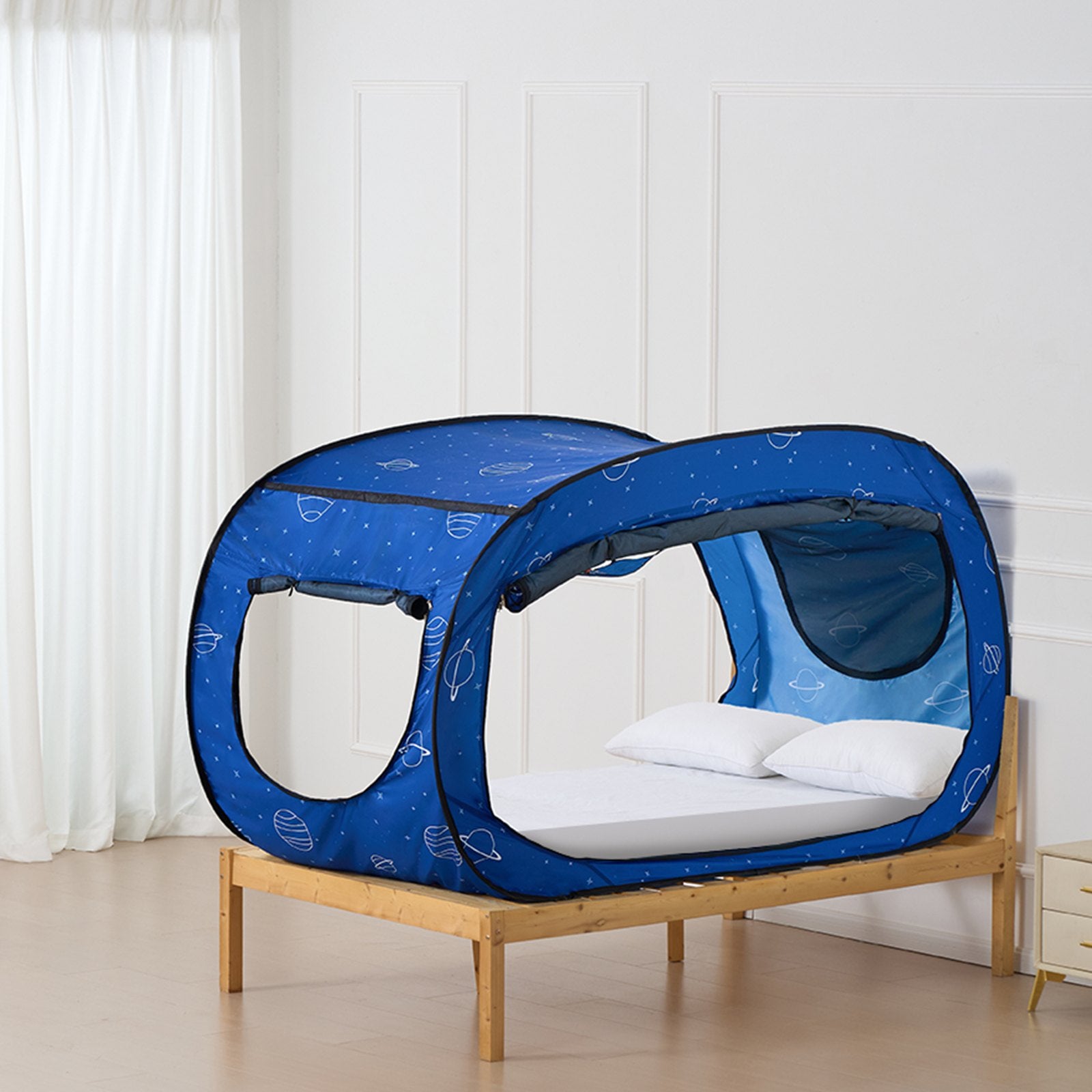Blue children's bed tent with white stars on a wooden bed against a white wall.