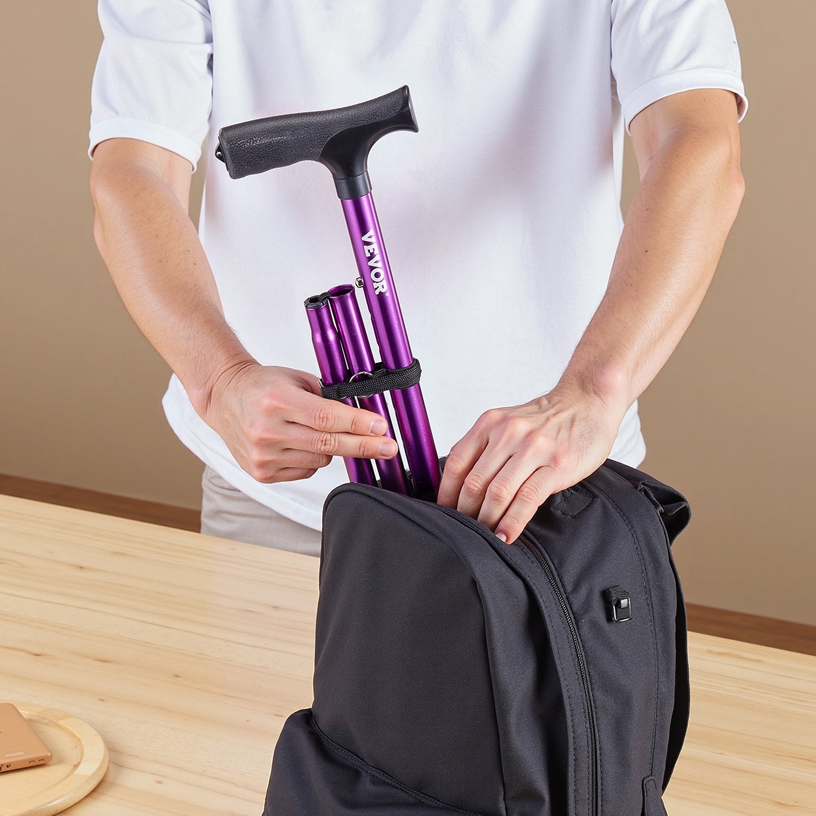 Person packing a purple walking cane into a black backpack on a wooden surface.