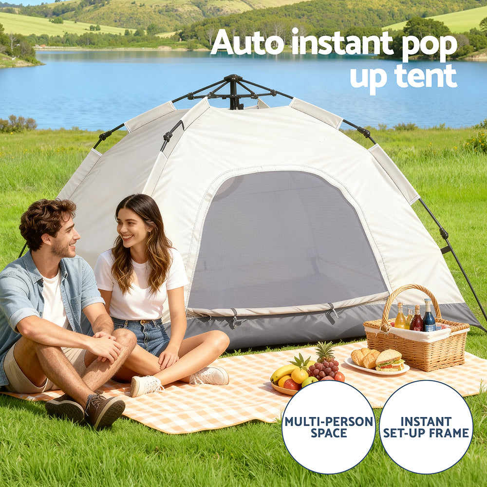 Two people sitting under a pop-up tent by a lake with picnic items on a blanket.