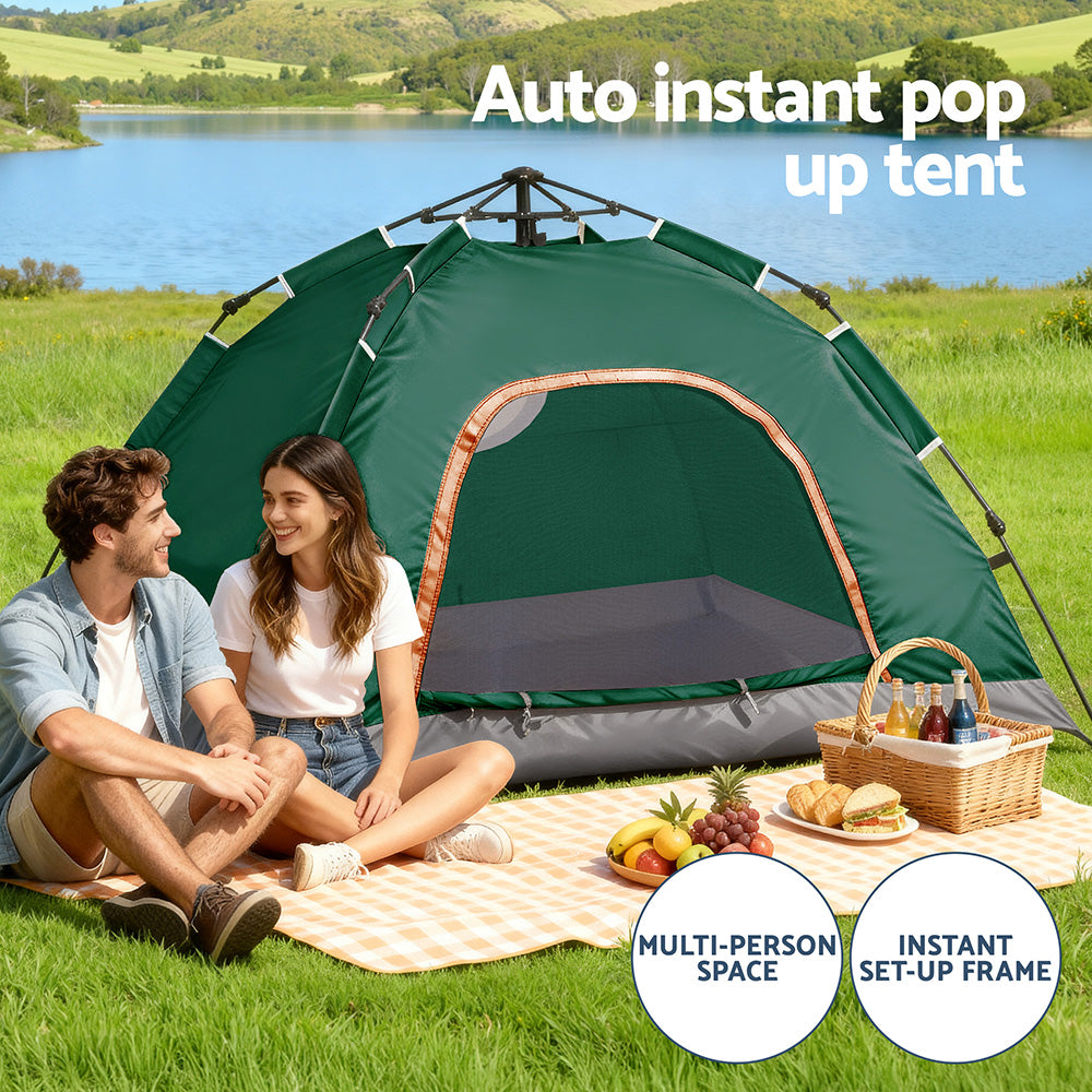 Two people sitting in front of an auto instant pop-up tent by a lake with picnic items.